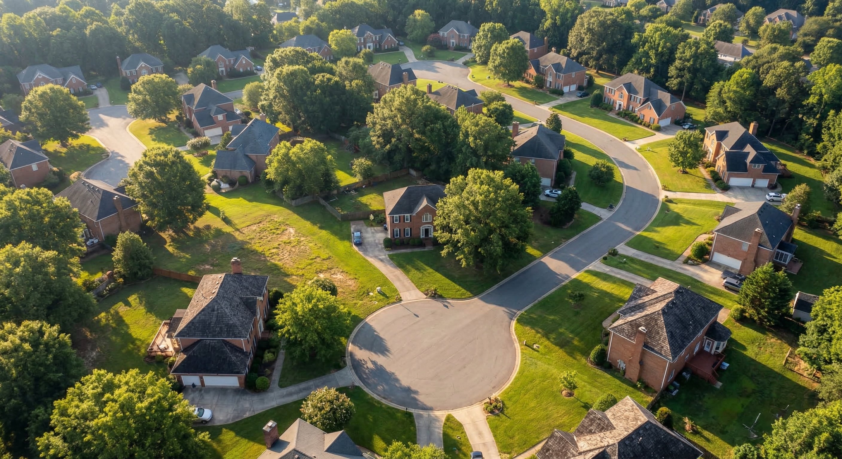 Aerial drone view of tree-lined residential streets in Charlotte, NC suburb with brick colonial homes and green lawns