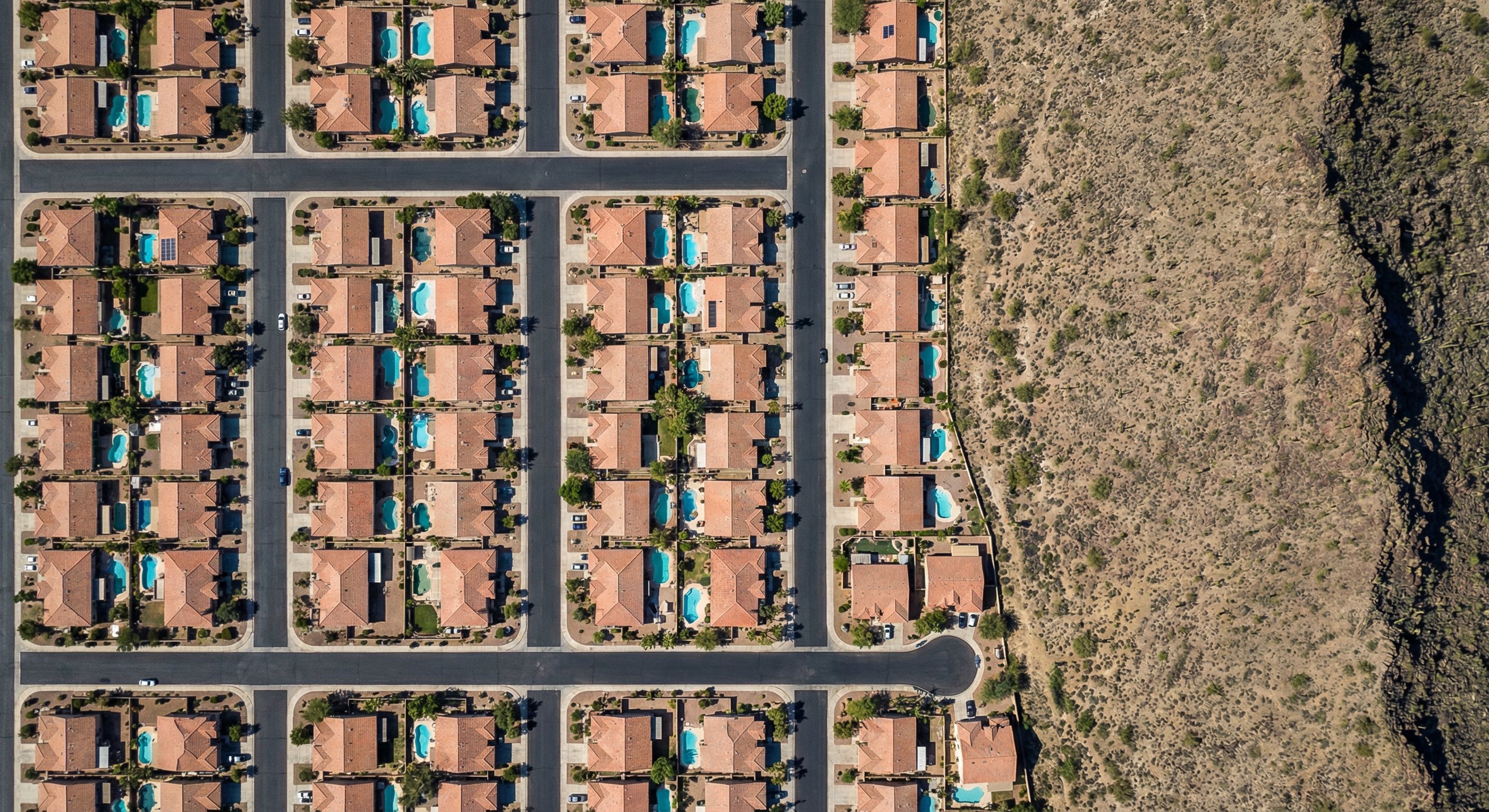 Aerial satellite view of Phoenix Arizona suburban neighborhood with swimming pools and mountain backdrop