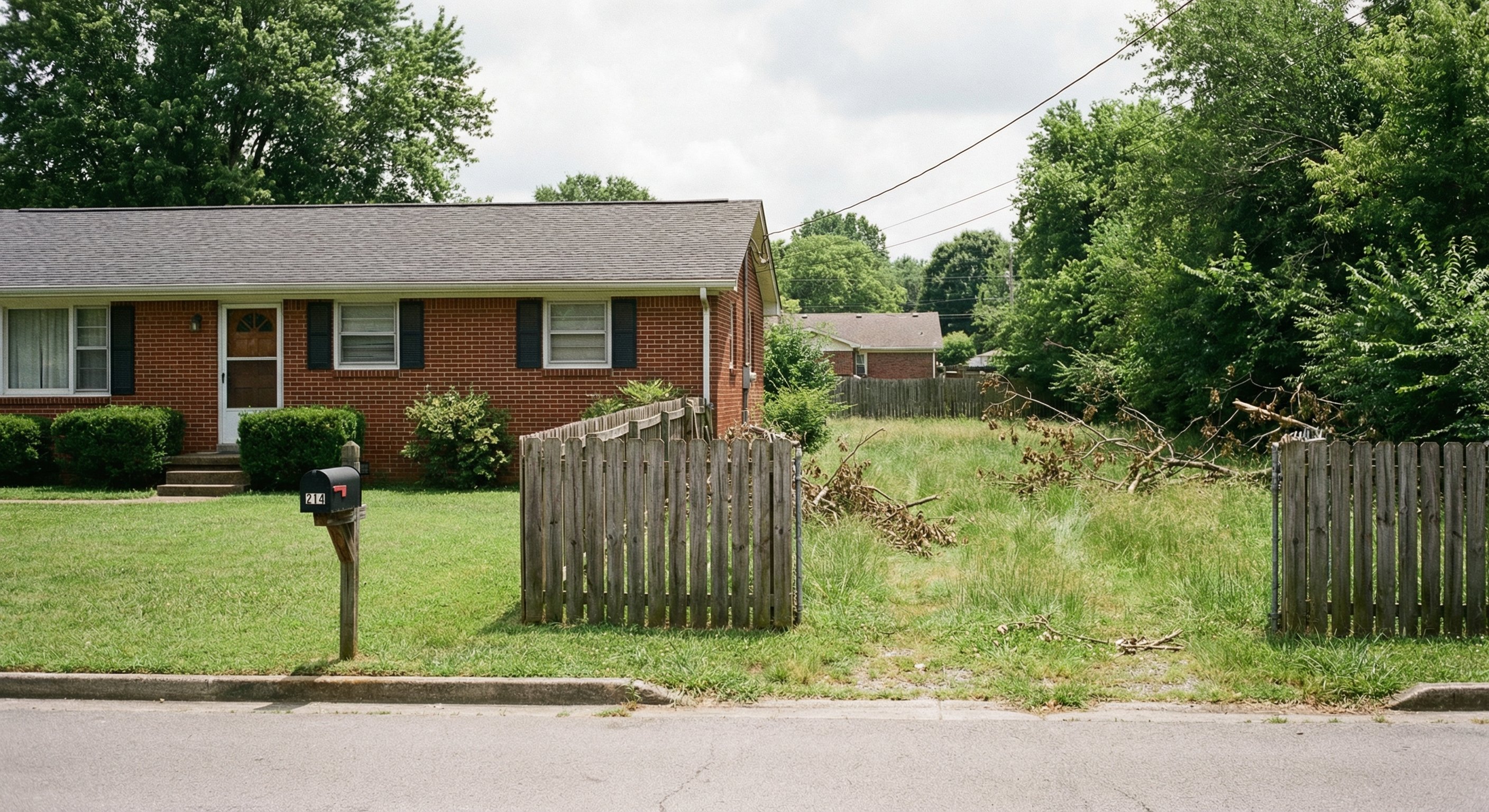 Tennessee brick ranch home with deferred yard maintenance visible through fence