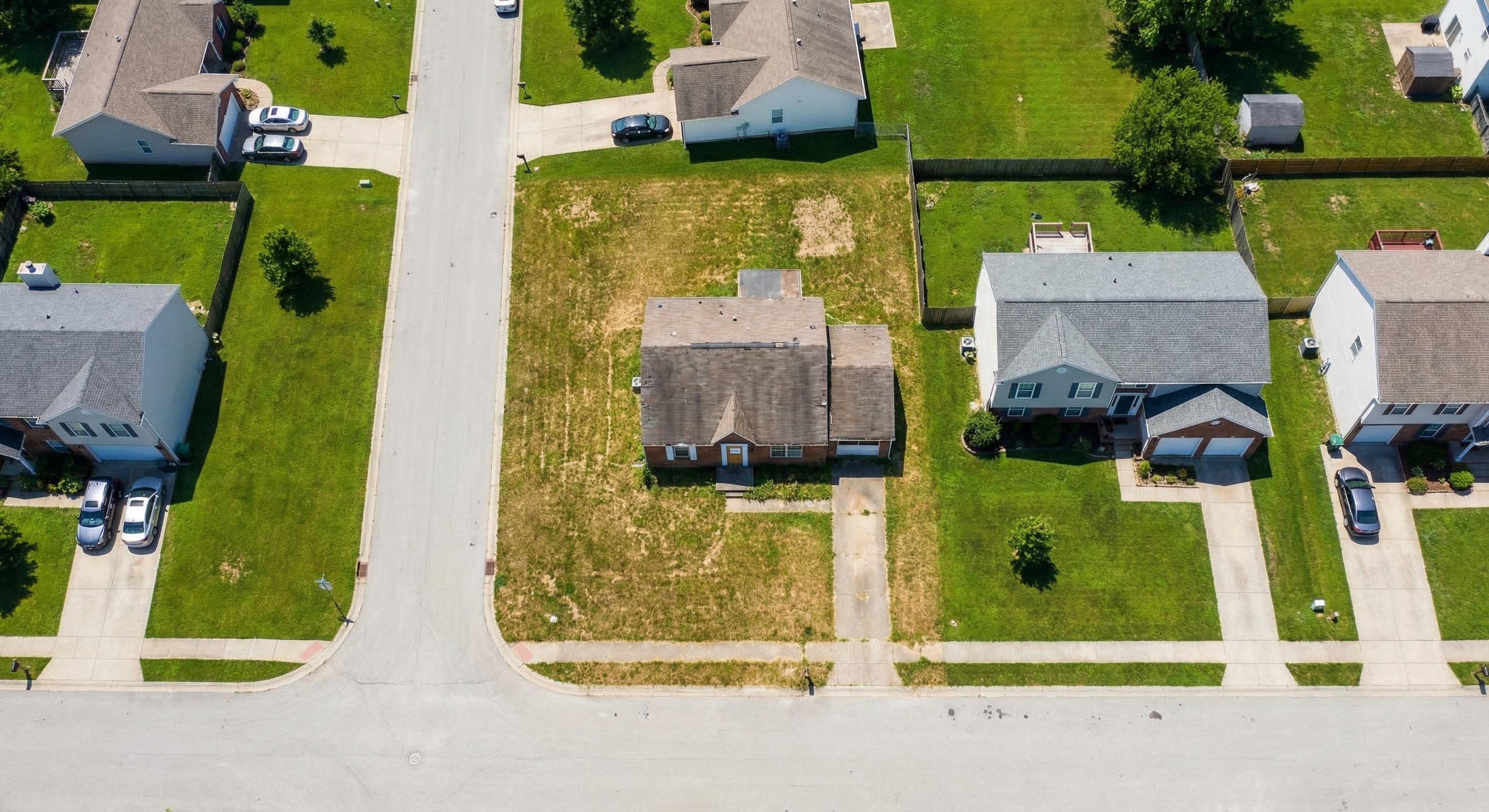 Aerial view of suburban neighborhood showing one neglected vacant property with overgrown lawn among well-maintained homes