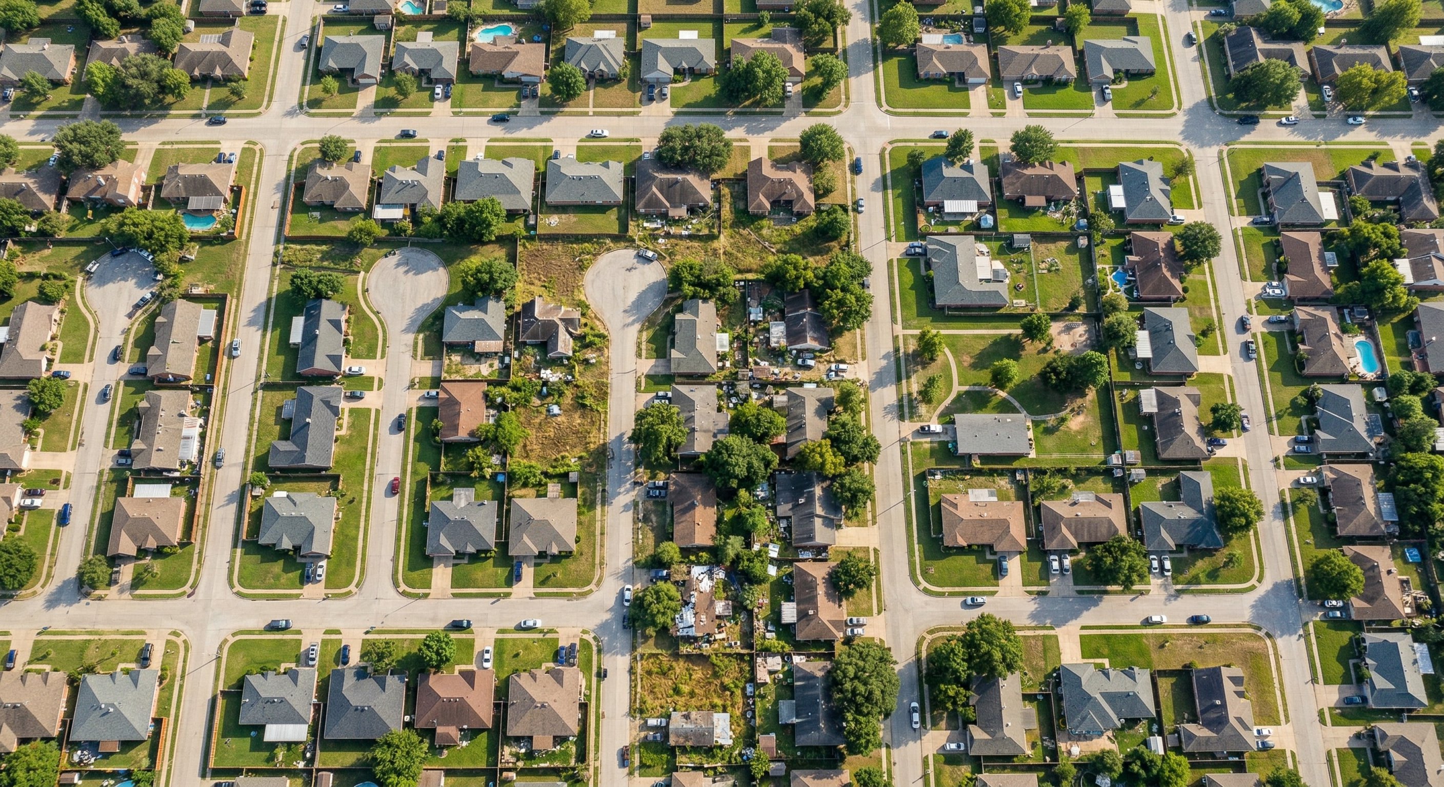 Aerial drone shot looking down at a suburban Texas neighborhood — grid of single-family homes with some showing signs of deferred maintenance, shot at 400 feet, warm afternoon sun, wide-angle DJI Mavic 3, real estate aerial photography.