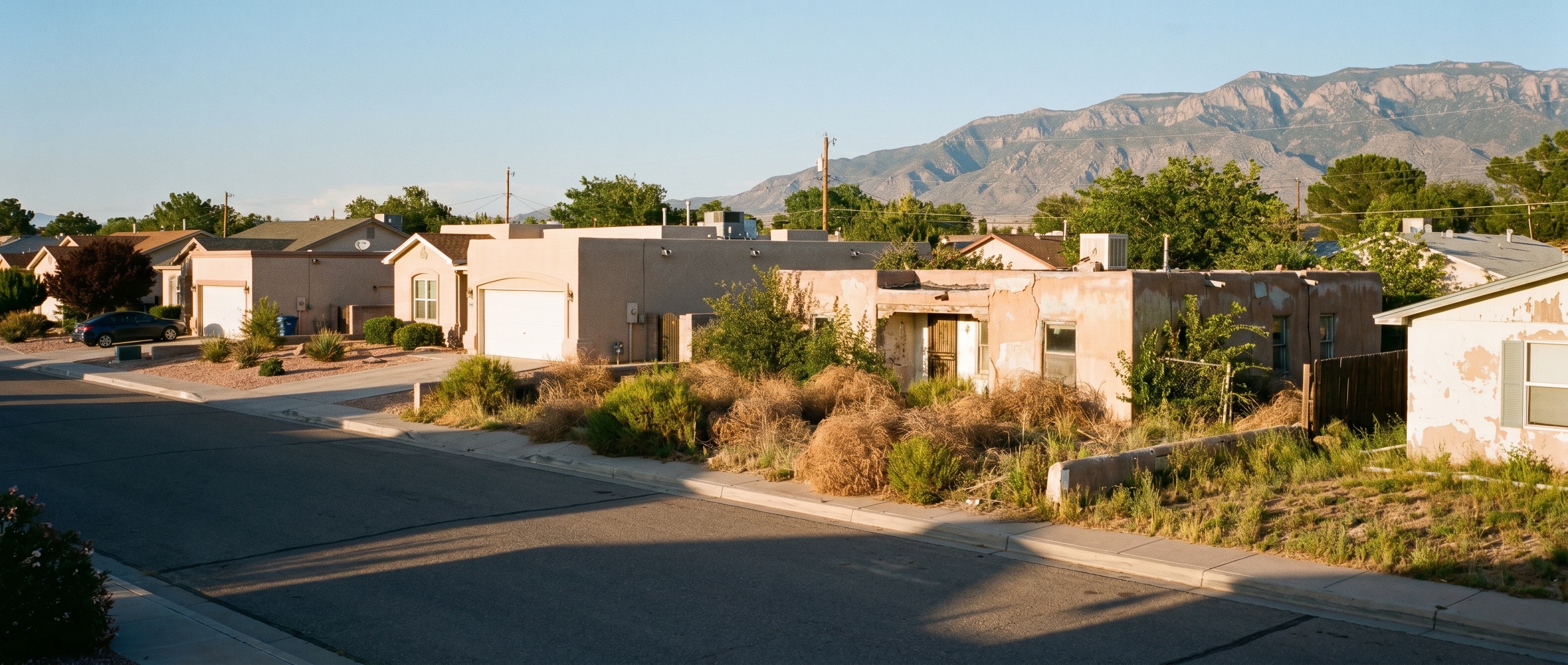 Wide cinematic shot of an Albuquerque New Mexico residential street with a mix of well-maintained and distressed properties, desert landscaping, afternoon shadows