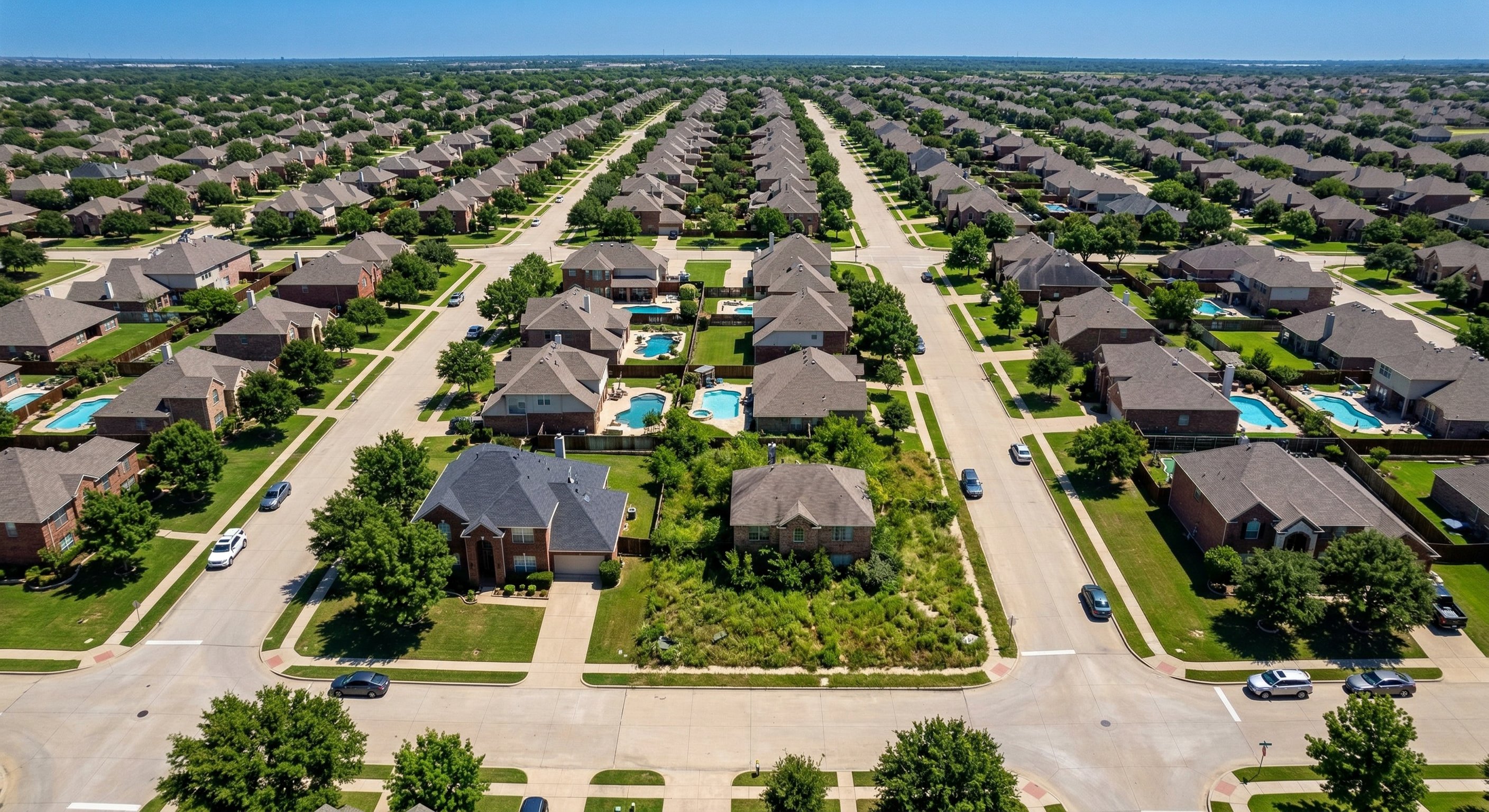 Aerial drone photograph looking down on a Texas suburban neighborhood with a mix of brick and stucco homes in a classic grid street layout, warm afternoon light