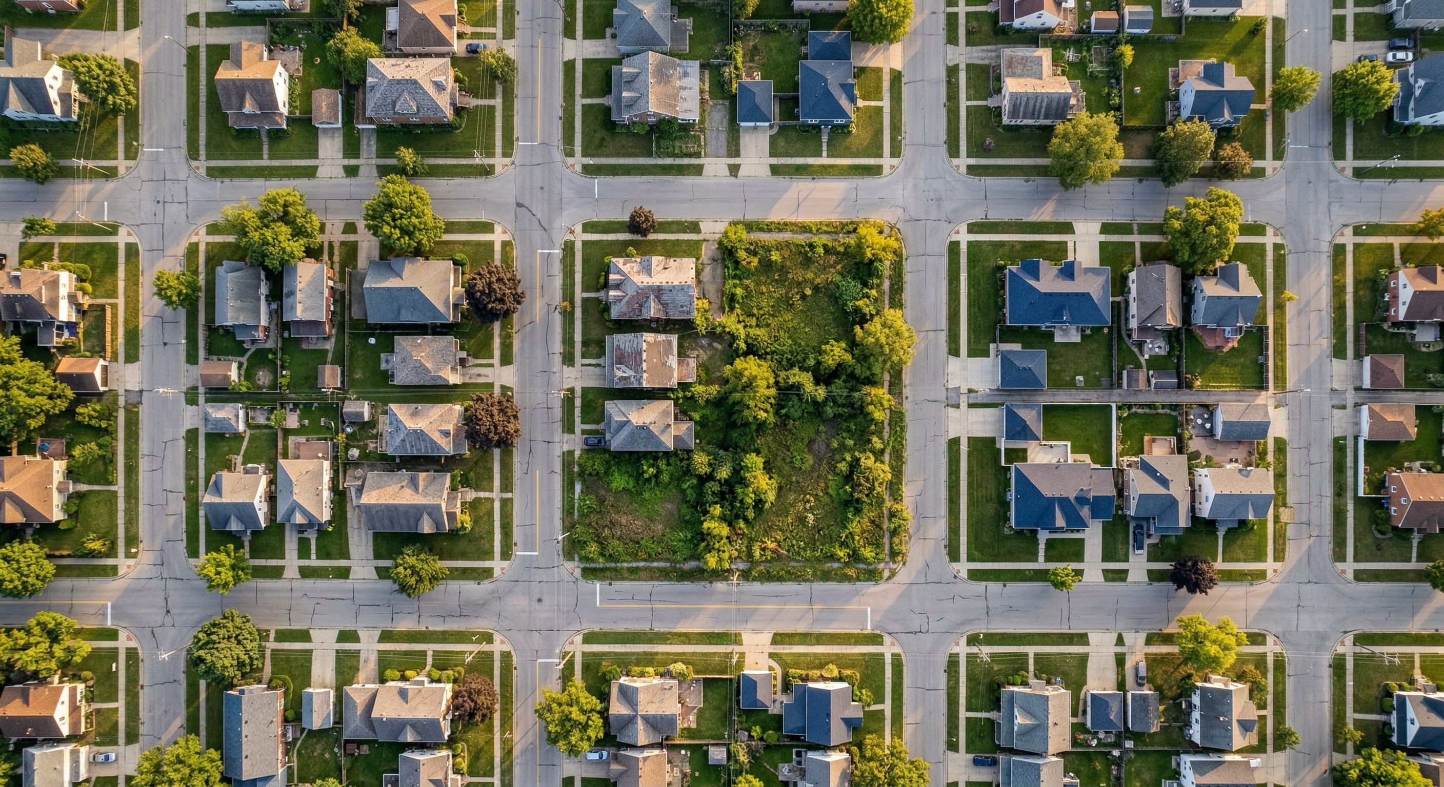 Aerial drone view of a mixed suburban neighborhood showing streets, rooftops, and vacant lots — an investor's view of the market