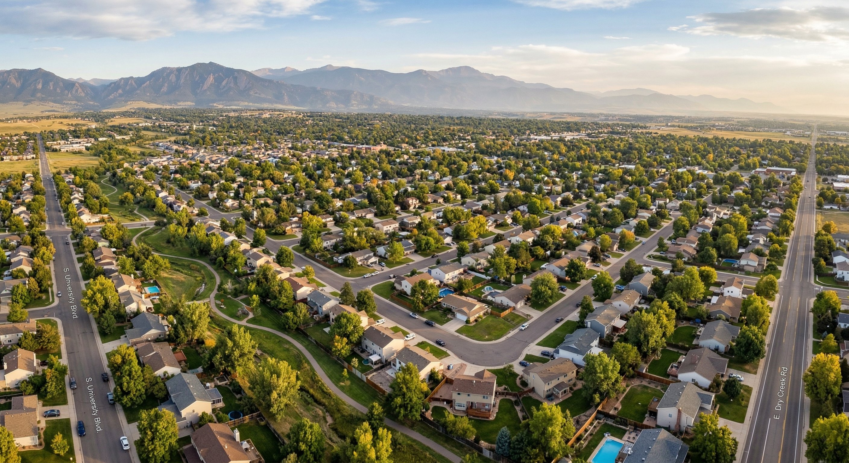 Aerial view of a Colorado Front Range residential neighborhood showing Denver-area suburbs, flat grid streets with mountains visible in the background, drone photograph, golden afternoon light, wide angle, real estate aerial photography