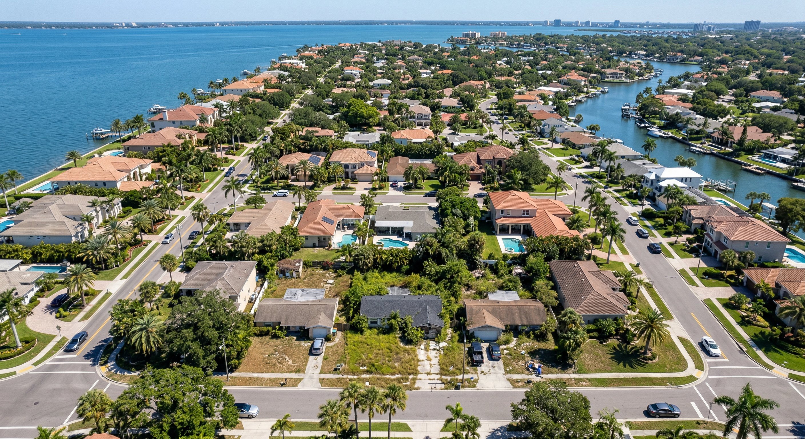 Aerial drone photograph of a coastal Florida residential neighborhood showing mix of maintained and distressed properties near Tampa Bay, clear blue sky