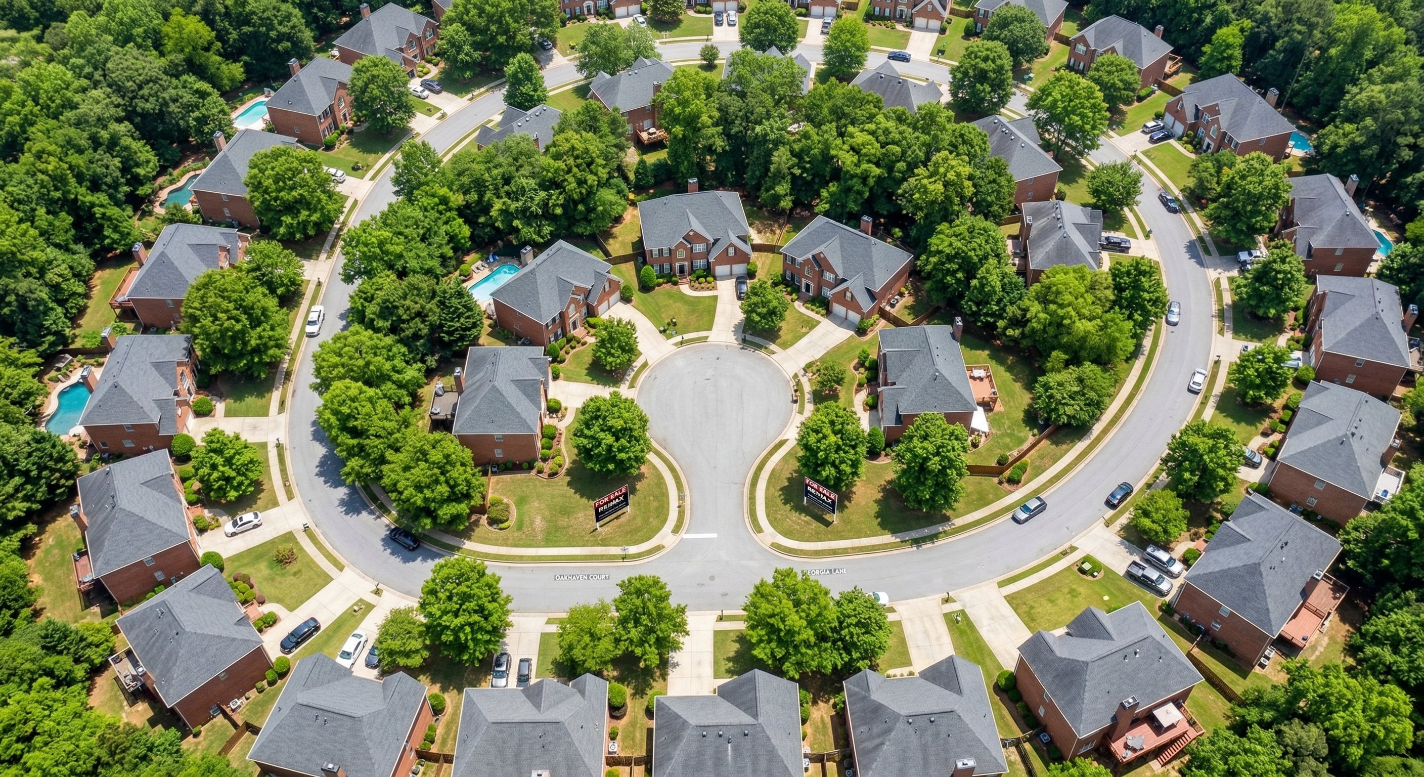 Aerial drone photograph of a residential neighborhood in suburban Atlanta, Georgia — consistent red-brick subdivision homes, cul-de-sac pattern, tree canopy starting to fill in, late morning light, real estate aerial photography
