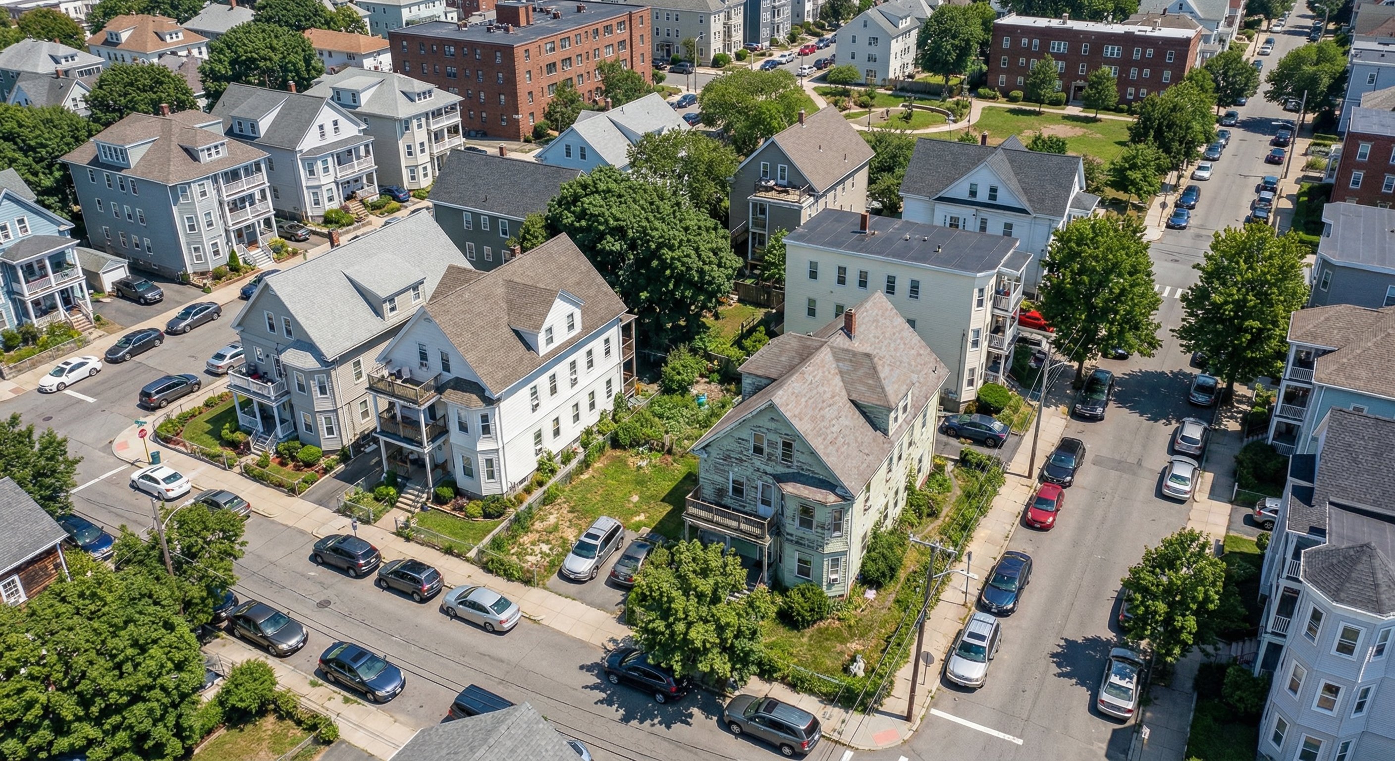 Low-altitude aerial of a dense Massachusetts urban neighborhood showing triple-decker homes and mixed property conditions