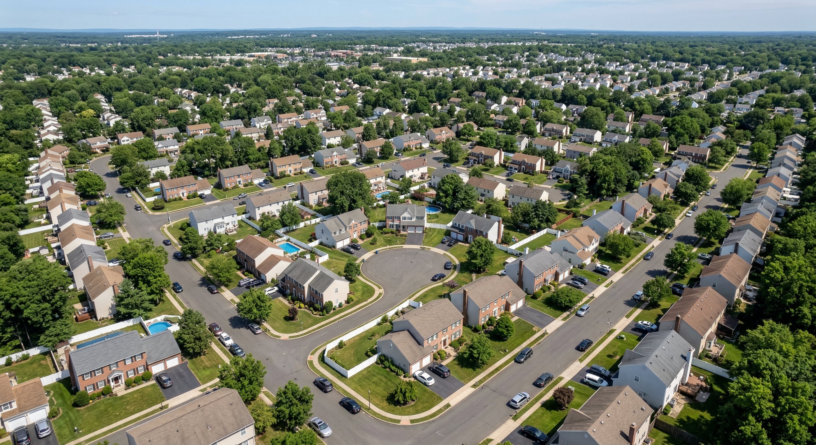 Aerial view of a dense New Jersey suburban neighborhood — Bergen County residential grid with varied colonial and split-level homes, mid-morning light casting soft shadows across the treetops, illustrating the scale of the NJ housing market