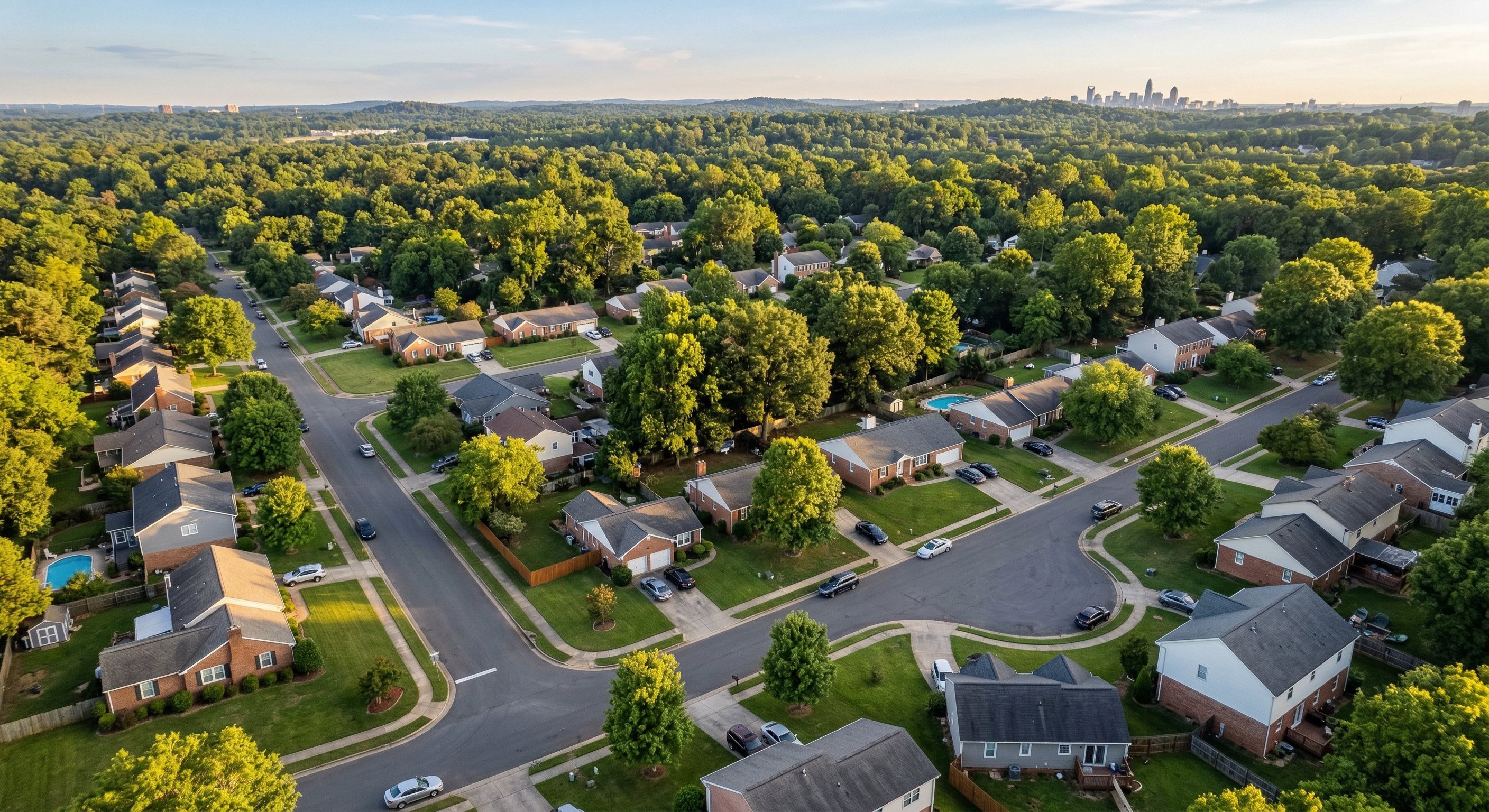 Aerial drone photograph of a Charlotte NC residential neighborhood, mix of single-family homes and tree-lined streets, warm late afternoon light, taken from 400 feet with DJI Mavic 3, wide angle lens