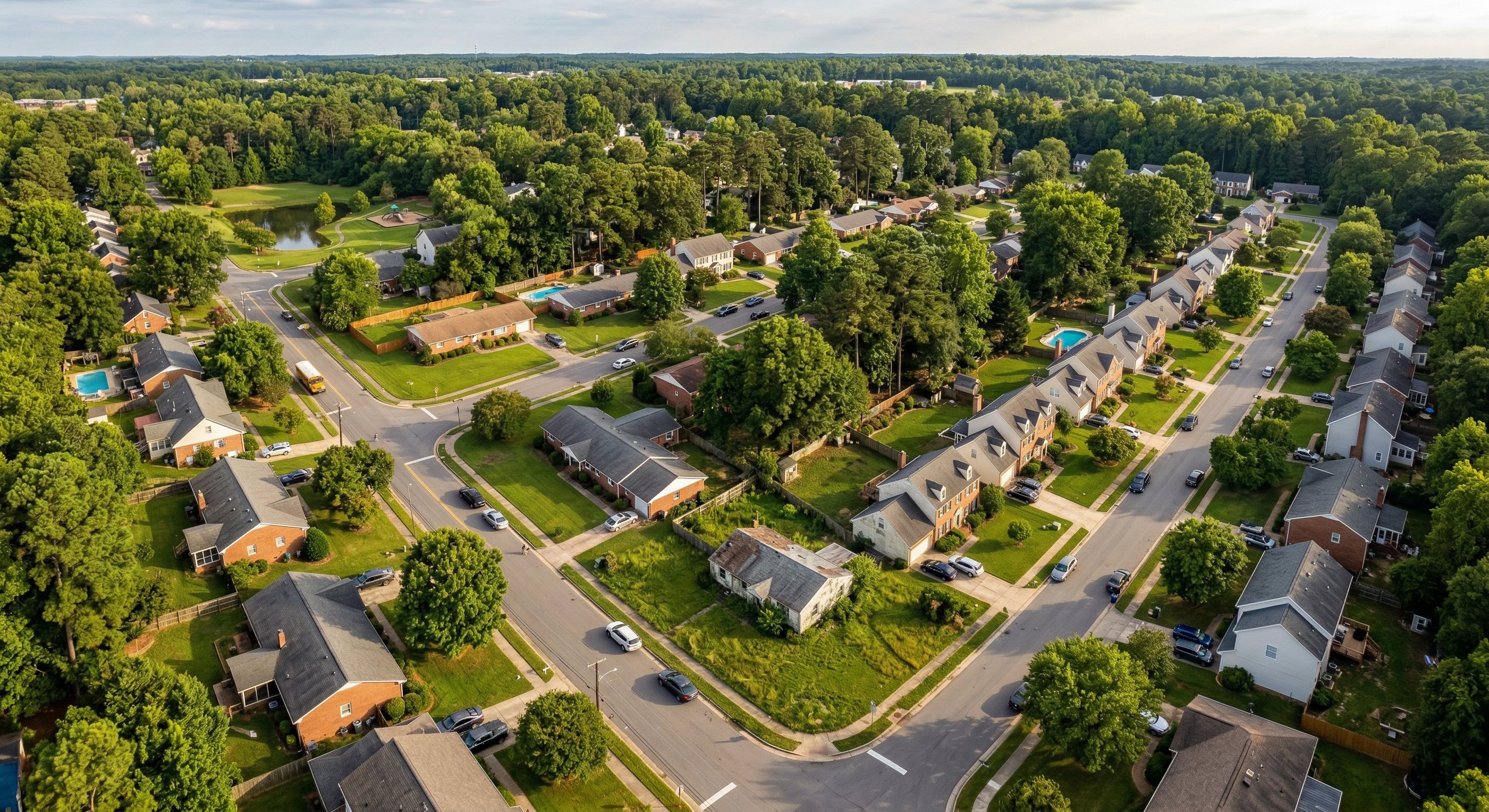 Aerial view of a North Carolina suburban neighborhood in the Research Triangle, tree-lined streets with mixed-era housing, warm afternoon light