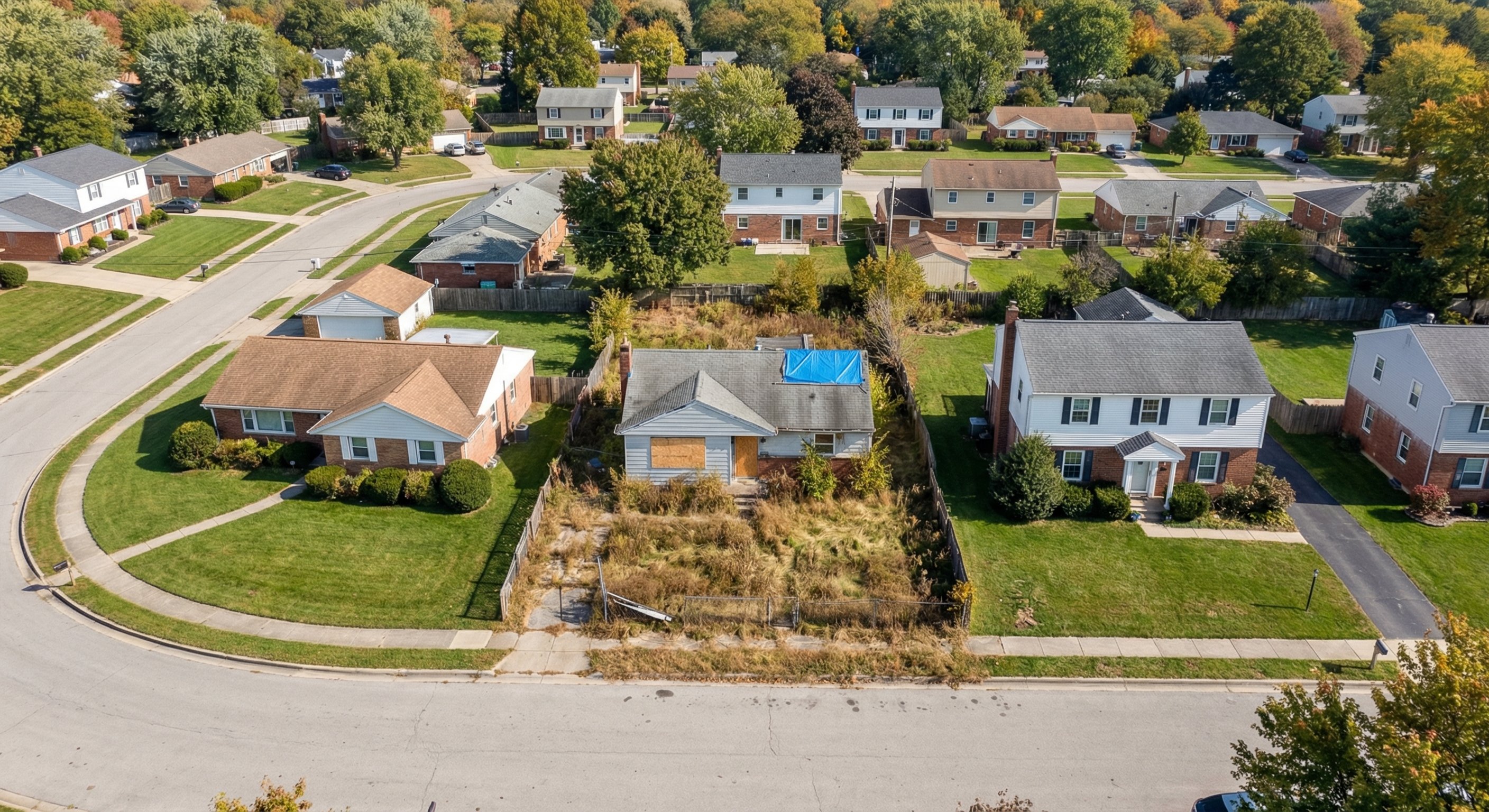 Low-angle aerial view of suburban neighborhood with one distressed vacant property visible