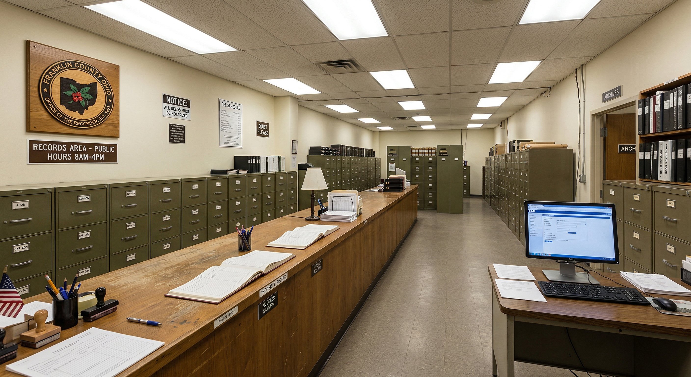 County recorder's office interior in Ohio — rows of filing cabinets with labeled drawers, institutional fluorescent lighting, a public records counter with informational signage, documentary photography style, natural color tones