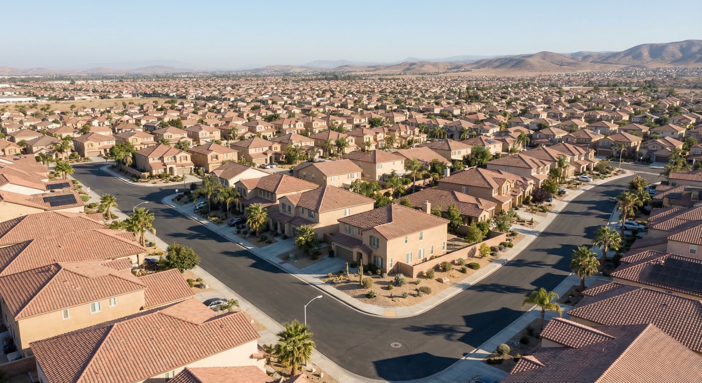 Aerial drone view of a Southern California suburban neighborhood showing residential streets with Spanish tile roofs and desert-adjacent landscaping, illustrating the scale of property inventory in the region