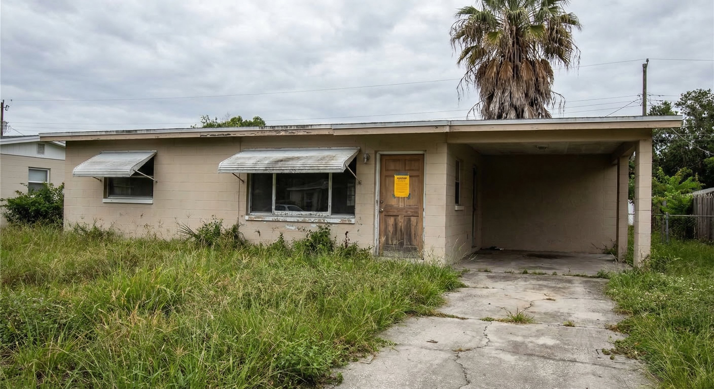 Neglected Florida concrete block home with county code enforcement notice on door, real estate documentary photography
