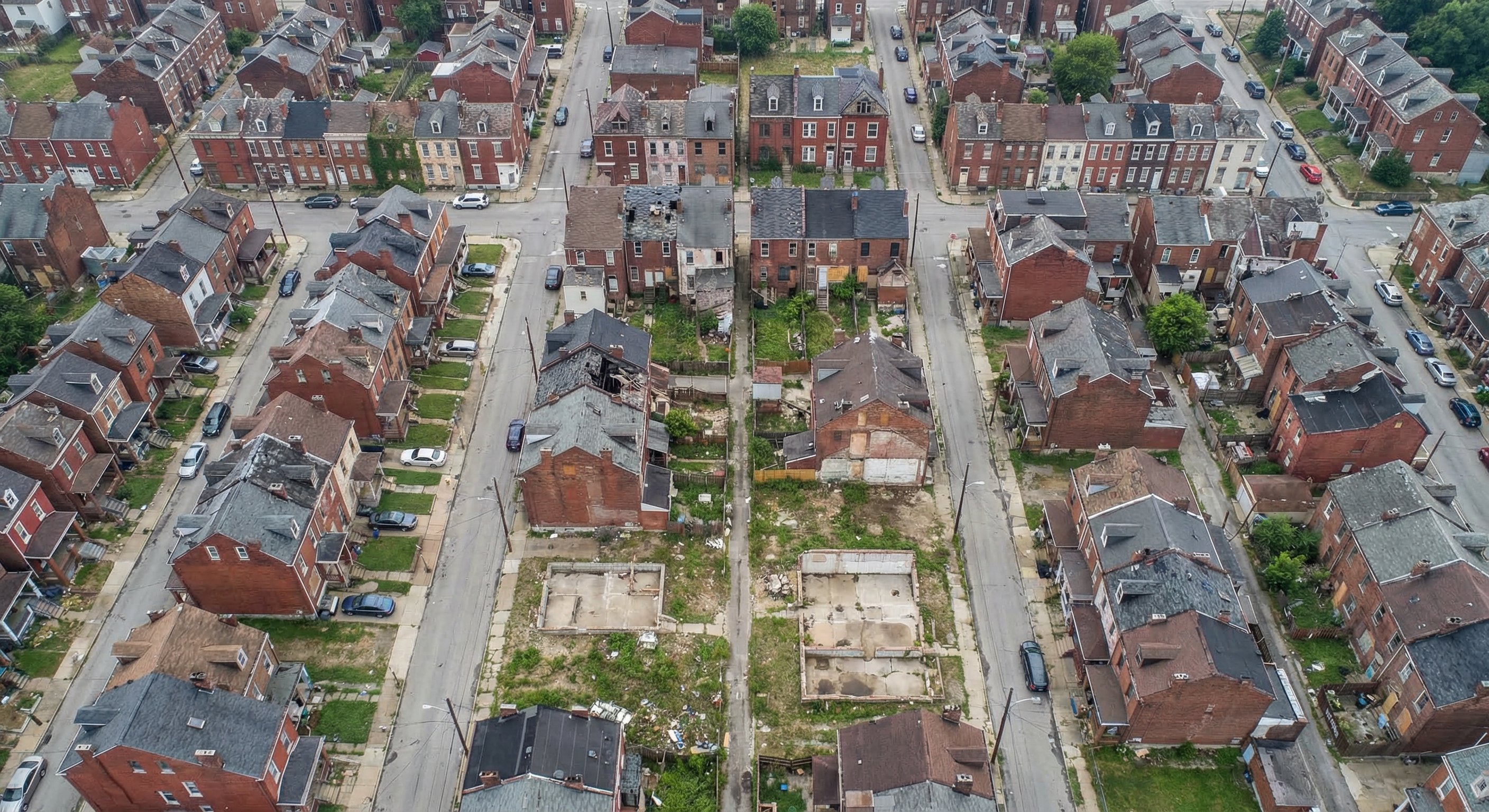 Aerial drone view of a dense older Pennsylvania neighborhood showing a mix of occupied and vacant row homes, brick two-story structures, and overgrown lots — typical Pennsylvania urban vacancy pattern