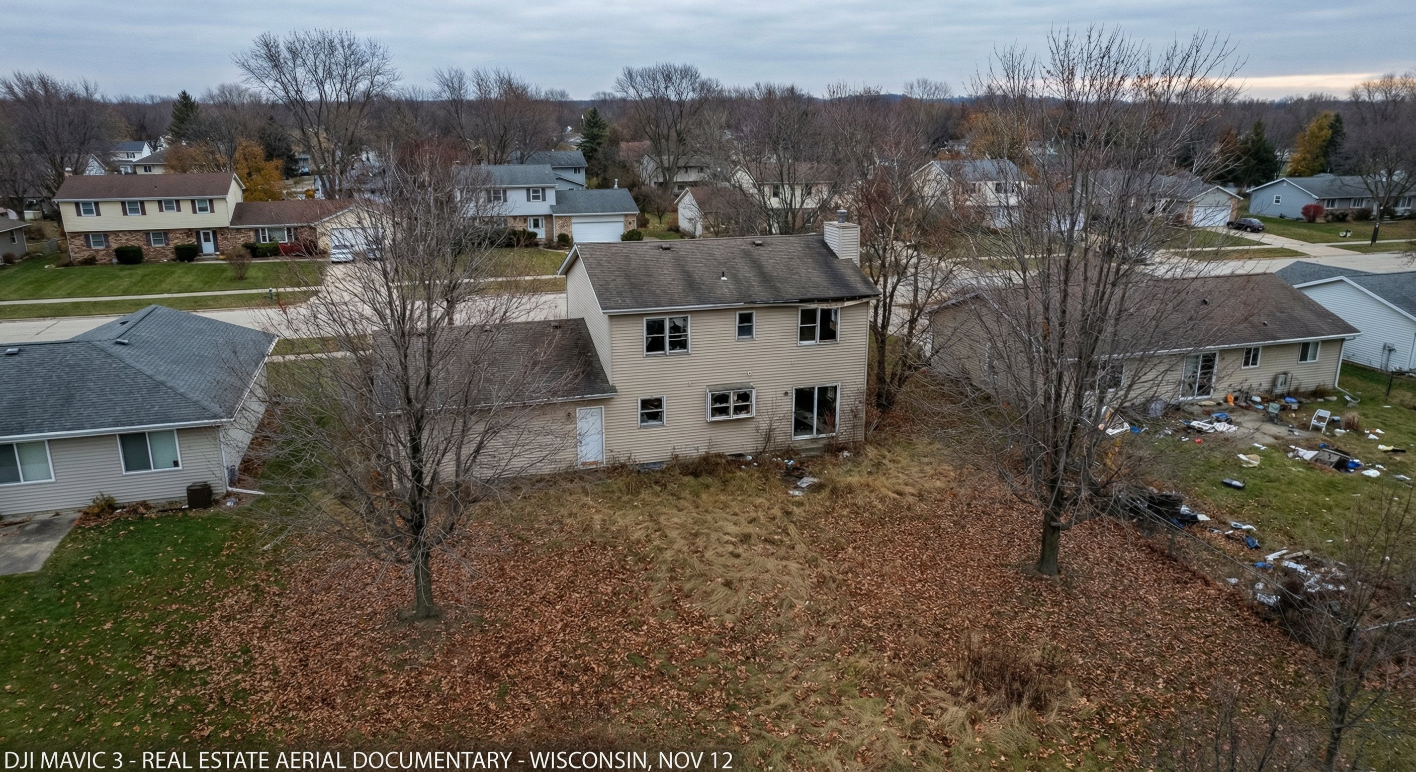 Aerial view of a vacant Wisconsin suburban home in late autumn showing neighborhood patterns of maintained versus neglected properties